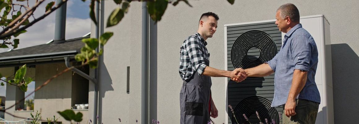 Zwei Personen schütteln sich vor einer Wärmepumpe die Hand